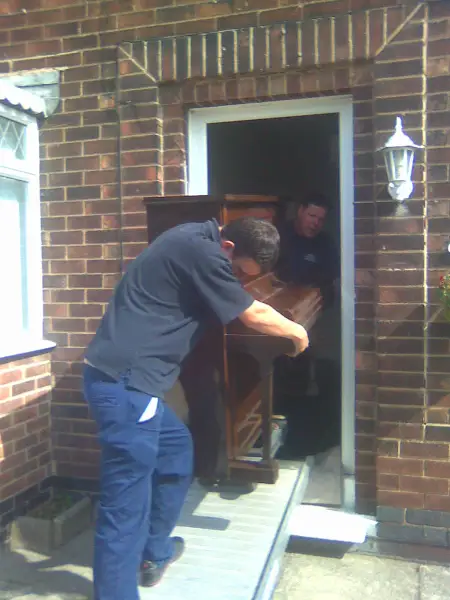 Piano Moving is never easy !
Even for one of the best in the business with Jonills.
And yes they usually have one our padded 
covers over them but often modern pvc doors
are to narrow so you have to take the cover 
off and use your 40 years  of skill to go through
a door with no damage to the piano
or the customers property !: Swipe To View More Images